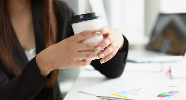 Close-up of woman with manicure hold cup of coffee, posing on working place in office. Break for lunch, enjoy drink, take pause. Chill, relaxation concept