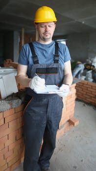 Portrait of busy professional worker hold clipboard and list needed work materials. Handyman wear uniform and protective helmet. Construction site concept