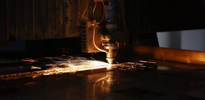 Close-up of sparks fly out of automated machine, metal processing laser on metallurgical background. Manufacturing, parts for automotive production concept