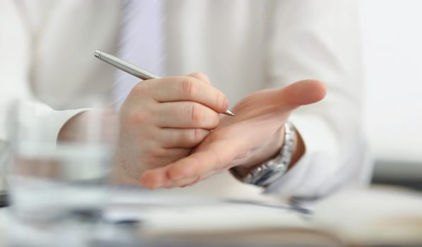 Close-up of male writing note with silver pen on his hand to keep in mind some information. Try not to forget, to do list, reminder. Note, memory concept