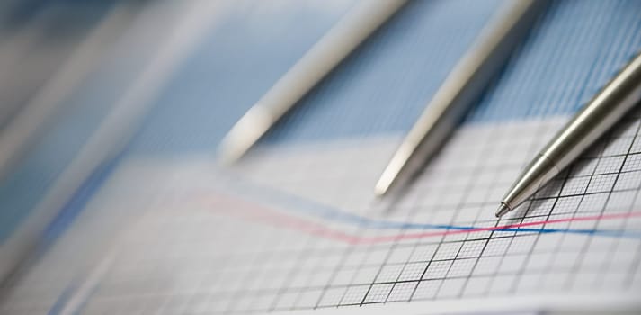 Close-up of business paper with graphic, blue and red line in increase and decrease order. Set of silver pens on top. Statistics, business, finance concept
