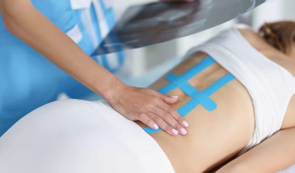 Close-up of woman doctor hold scan of woman back and correct kinesiology tape on females body. Treatment for faster recovery after injury. Health concept
