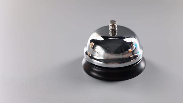 Close-up of silver bell stands on grey surface to attract attention, press bell to call service. Thing to put on reception. High quality service concept