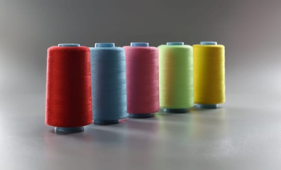 Close-up of group of whole haberdashery item colorful thread spools on grey surface. Colorful bobbins for tailoring. Dressmaking, atelier, fashion concept