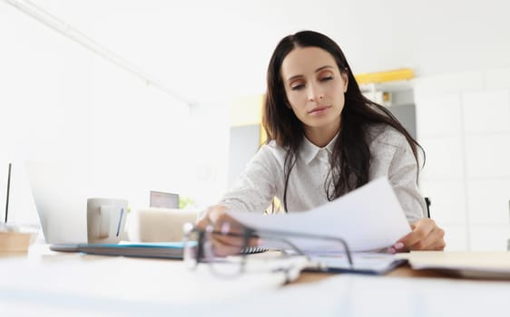 Portrait of tired overworked young woman go through paper on working place. Exhausted employee in office. Hardworker, businesswoman, workaholic concept