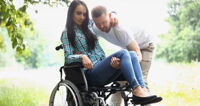 Portrait of man husband take woman in arms, disabled wife on wheelchair. Male partner visit in hospital. Disability, nursing house, care, recovery concept