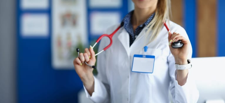 Close-up of female medical worker in white uniform posing with stethoscope on neck. Young woman specialist in office. Healthcare, appointment, help concept