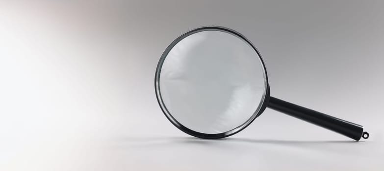 Close-up of single magnifying glass with black handle, leaning on grey surface. Simple design of lens or loupe to enlarge objects. Magnifying lens concept