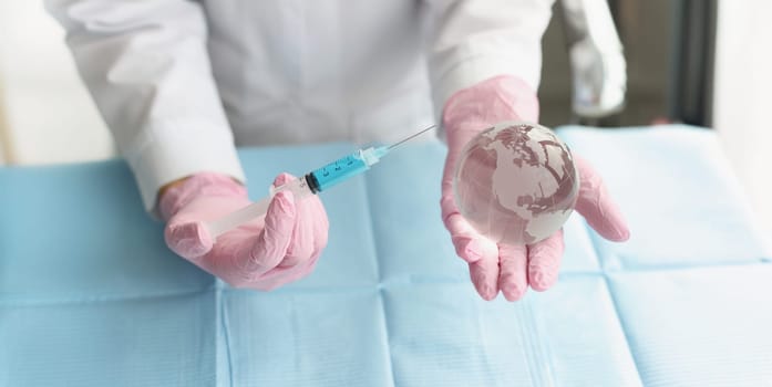 Close-up of medical worker hold syringe and miniature world globe in hands. Coronavirus injection, vaccination. Stop pandemic, shot, immunization concept