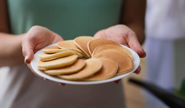 Close-up of woman holding plate with tasty fresh homemade pancakes. Hot delicious meal for breakfast, nutritious food to start day. Food, eating concept