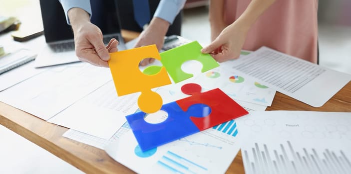 Close-up of coworkers solving jigsaw puzzle on workplace, colourful parts. Put puzzles into one, whole picture. New idea search, mind development concept