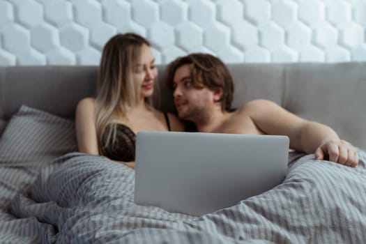 Couple watching porn movie over laptop in bedroom .