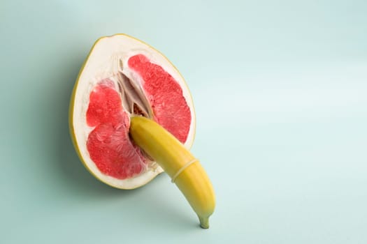 Safe sex. Juicy grapefruit and banana in a condom. The symbol of the vagina and penis from fruit.
