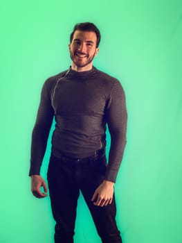 A man is standing in front of a vibrant green wall, with a smile. The wall provides a bright contrast to his dark clothing, creating a visually striking scene.
