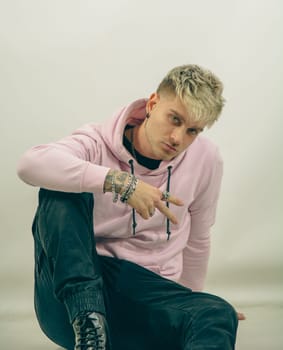 A man wearing a pink hoodie is doing the V sign for victory with his hand.. His arm is extended, and he seems to be directing attention towards a specific object or direction.