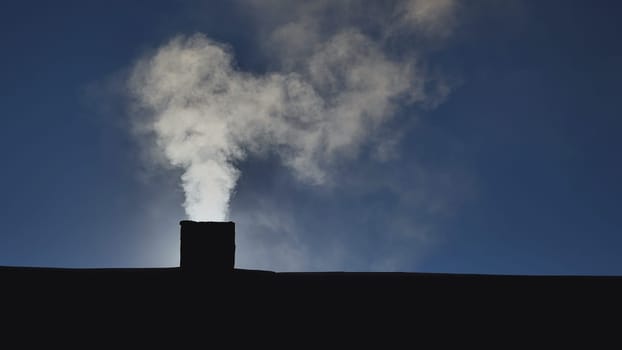Silhouette of smoke against the sun from the chimney of a village house