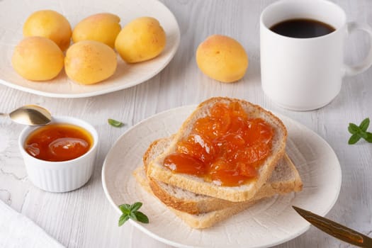 Apricot jam on bread in a white plate and a jar of apricot jam.