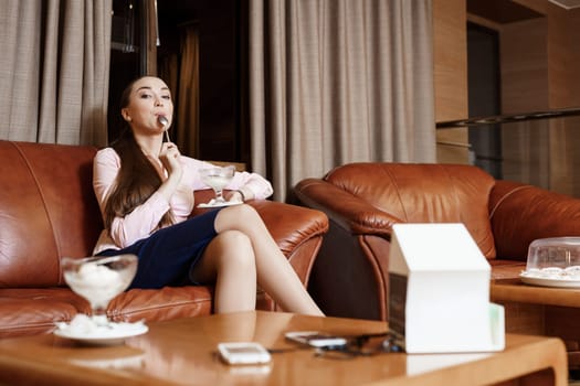 Young sexy brunette sitting in hotel lobby having dessert erotically licking spoon