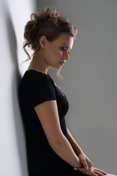 Young pretty blonde in black sexy tshirt with deep decollete posing in studio by the white wall