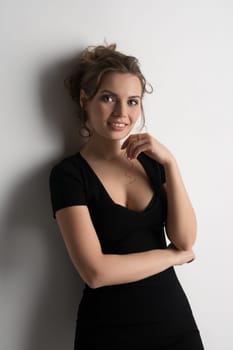 Young pretty blonde in black sexy tshirt with deep decollete posing in studio by the white wall with a tender smile
