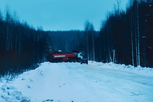 Timber truck full of wood driving along snowy road in winter forest