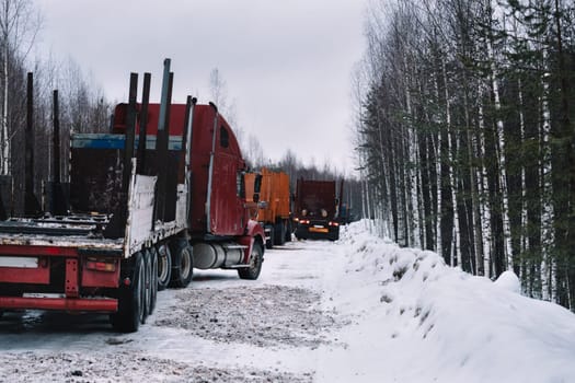 Unloaded convoy of long vehicles mooving on winter road among forest