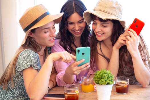 Group of smiling multiethnic women enjoying vacation in a restaurant. Beautiful and cheerful Generation Z girls browsing the internet with smartphones