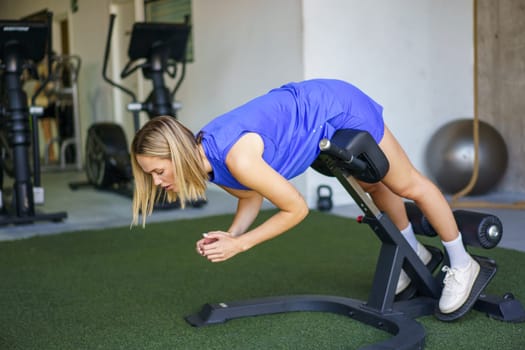 Horizontal photo with copy space of a blonde young caucasian fitness woman doing incline sit-up exercises in the gym