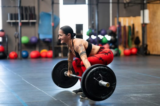 Mature sportive woman in squat position to lift weight in a gym