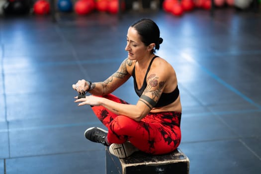 Sportive strong mature woman sitting on a box protecting her fingers with tape in a gym