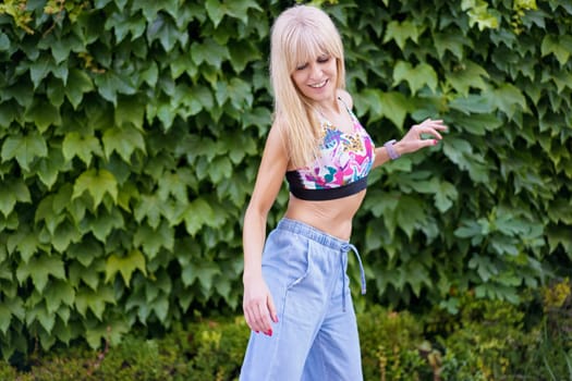 Cute female caucasian blonde dancer in casual summer clothes dancing next to garden outdoors in a sunny day