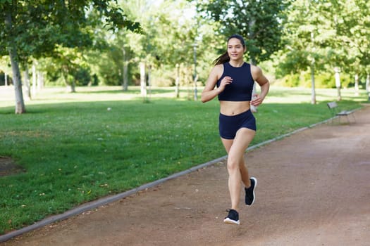 A young woman runs in a green park, embracing fitness and health. Ideal for conveying themes like lifestyle, exercise, and wellness. Keywords active, health, fitness, outdoors, wellbeing