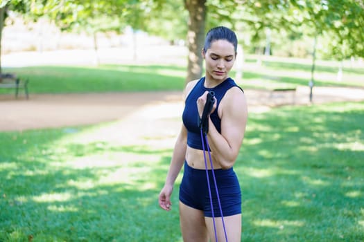 Athletic woman in sportswear exercising with resistance bands in a scenic park setting, showcasing strength and fitness