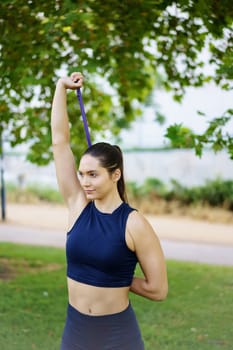 In a serene green park, an athletic woman in activewear is engaged in outdoor strength training using a resistance band. Fitness and wellbeing are essential in her workout routine