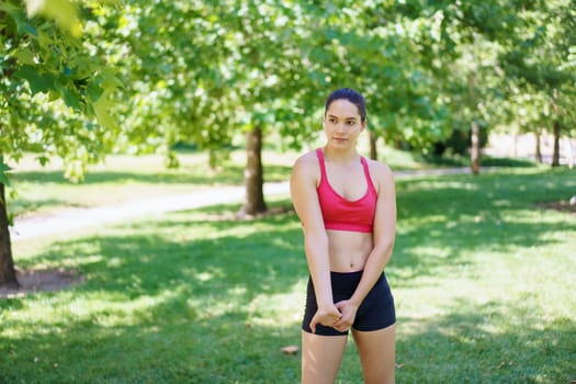 In a lush green park, a determined young woman in pink sports bra and black shorts is deeply focused on her exercise routine, displaying energy and dedication amidst natures beauty