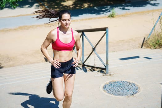 A young woman in a pink top and black shorts displays dedication to fitness by jogging outdoors on a sunny day in a natural exercise environment, showing her commitment to a healthy lifestyle