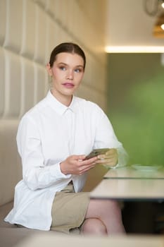 Vertical photo of a beauty businesswoman using phone sitting in a cafeteria