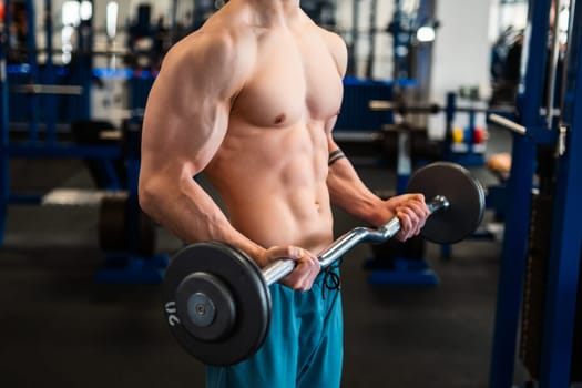 A muscular bodybuilder performs bicep curls with a barbell in a gym
