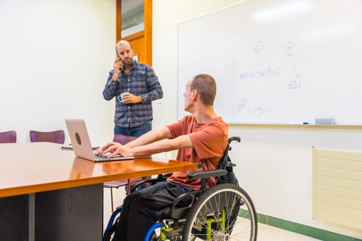 Caucasian man with disability and a work colleague working using laptop during a creative process in a coworking