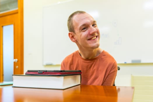 Happy man with disability sitting in an university classroom using digital tablet to study