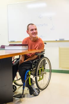 Vertical photo of a man with disability in a wheelchair in the university using tablet to study