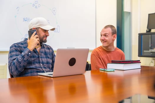 Man with cerebral palsy working using laptop and tablet with a colleague in a coworking