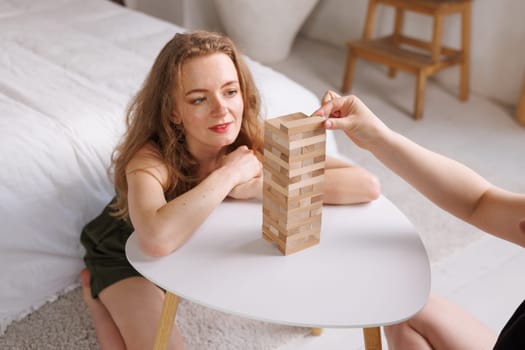 two women playing a board game made of wooden blocks at home, excitement and relaxation, mind development concept, hand motor skills,