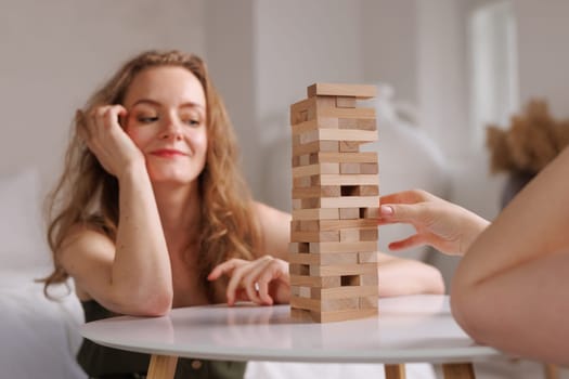 two women playing a board game made of wooden blocks at home, excitement and relaxation, mind development concept, hand motor skills,