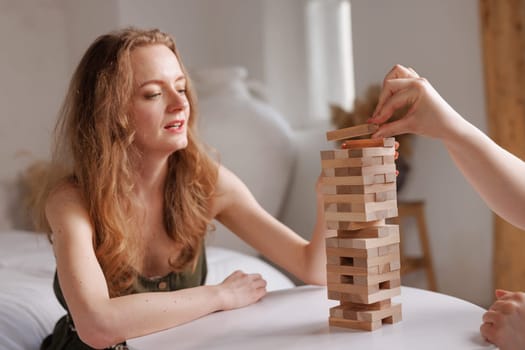 two women playing a board game made of wooden blocks at home, excitement and relaxation, mind development concept, hand motor skills,