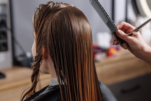 beauty master combing client's wet hair in beauty salon close-up, self-care concept, professional hair care