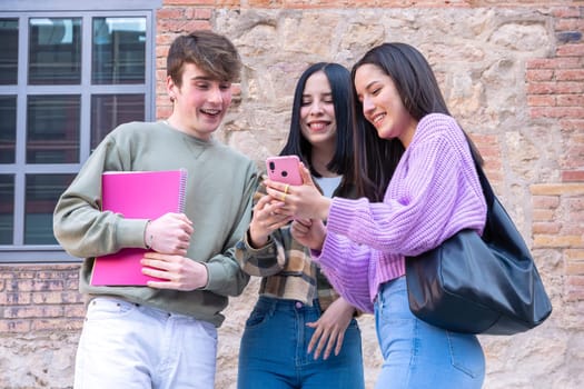 Happy multiracial students sitting outdoors using cell phone to chat online. University life concept