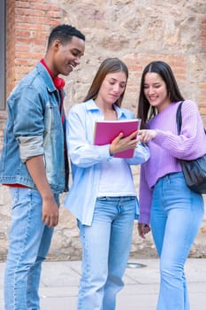 Happy multiracial university student friends talking and laughing while reviewing syllabus notes on campus. Diverse American and European youth.Vertical