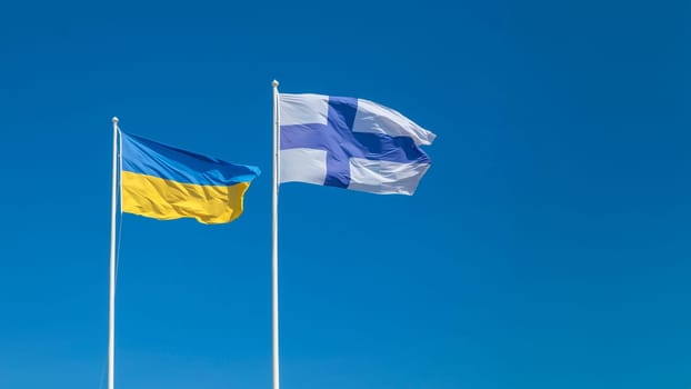 Ukraine and Finland waving in wind and sunlight flags on the clear blue sky, alliance and meeting, cooperation of states. National symbol of freedom and independence