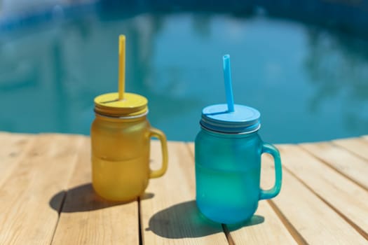 two cocktails of yellow and blue standing by the pool. Pool party outdoors.